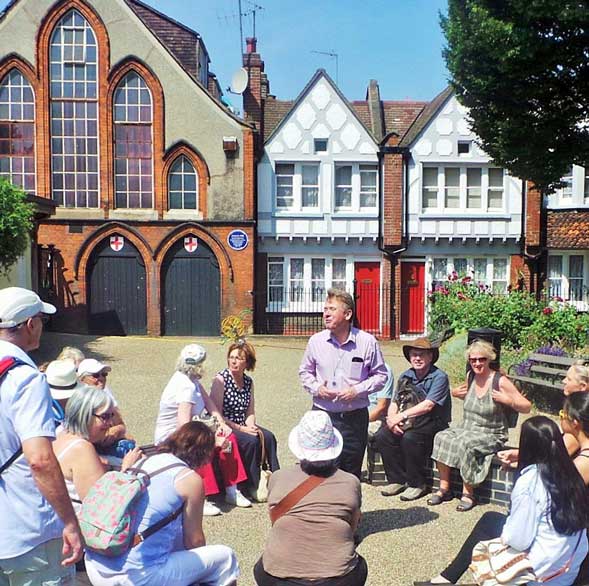 A group of walking tour participants sit down on benches as Richard tells them about their surroundings.