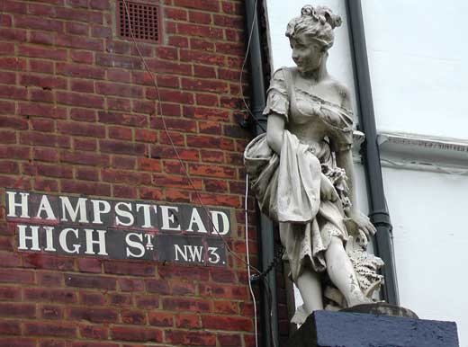 The Hampstead High Street sign with a statue of a lady to its right.